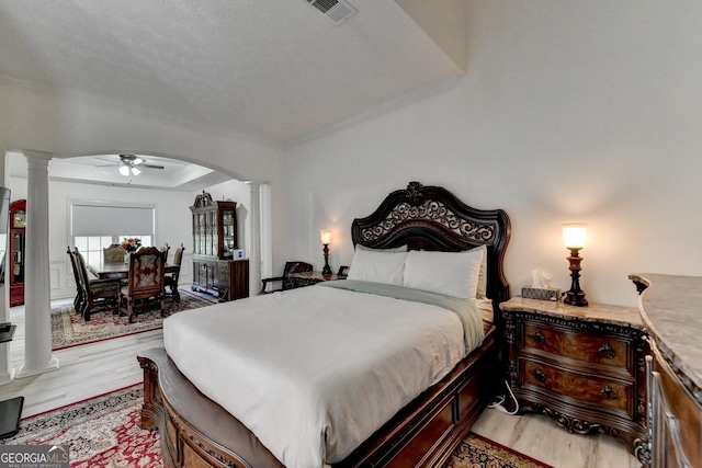 bedroom featuring arched walkways, light wood-style floors, visible vents, and decorative columns