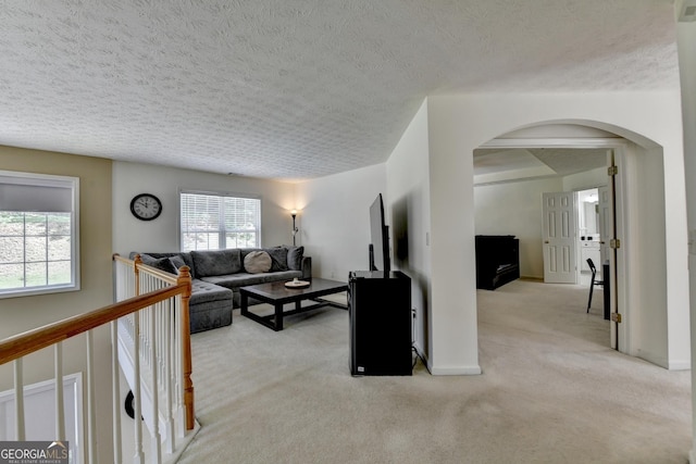 living room with a textured ceiling, carpet, arched walkways, and baseboards