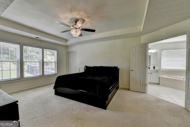 bedroom with a tray ceiling, ensuite bathroom, visible vents, ceiling fan, and light colored carpet