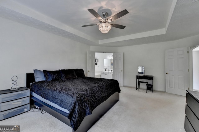 bedroom with a sink, light colored carpet, ensuite bath, a ceiling fan, and a raised ceiling