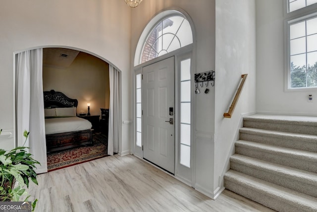 entrance foyer featuring stairway, baseboards, arched walkways, light wood-style floors, and a high ceiling