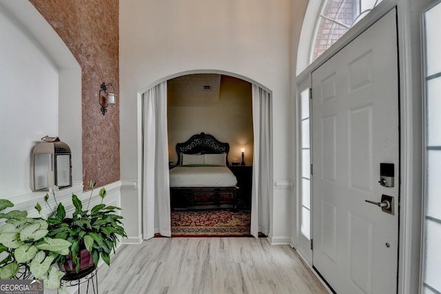 entryway with light wood-type flooring, plenty of natural light, a high ceiling, and arched walkways