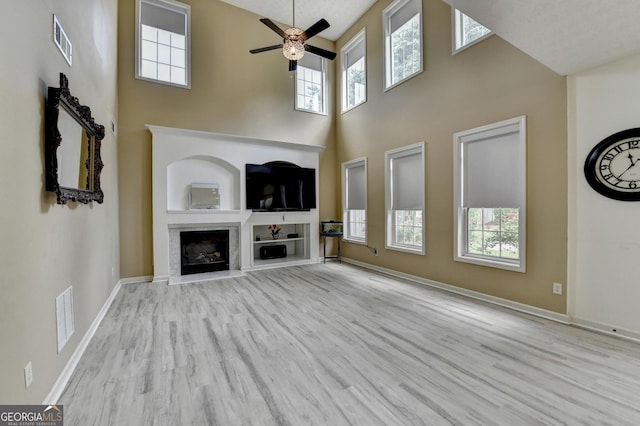 unfurnished living room featuring a ceiling fan, visible vents, a high ceiling, and wood finished floors
