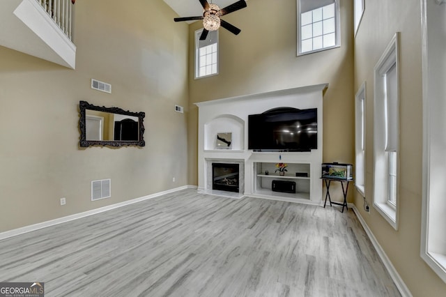 unfurnished living room featuring a towering ceiling, visible vents, and wood finished floors