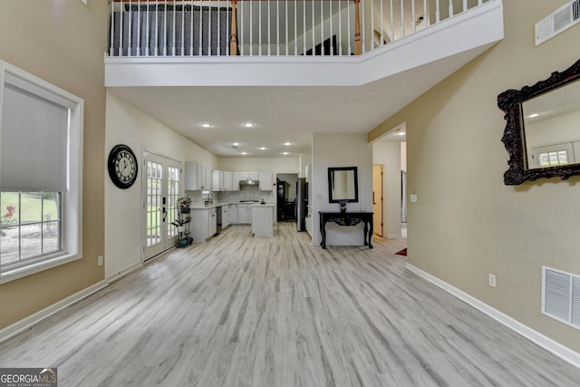 unfurnished living room featuring light wood finished floors, a high ceiling, baseboards, and visible vents