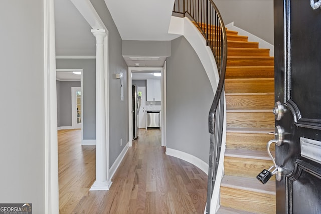 foyer featuring baseboards, ornamental molding, decorative columns, stairs, and wood finished floors