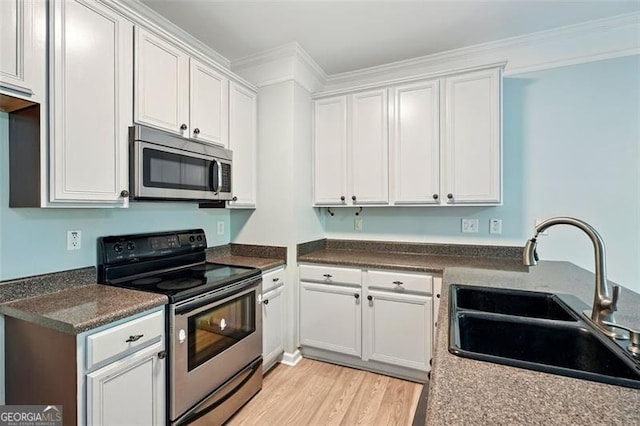 kitchen with a sink, stainless steel appliances, light wood-style flooring, white cabinetry, and dark countertops