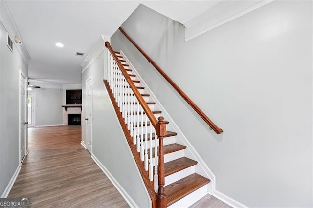stairs featuring baseboards, ornamental molding, a fireplace, and wood finished floors
