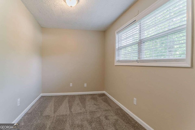 empty room with carpet, a textured ceiling, and baseboards