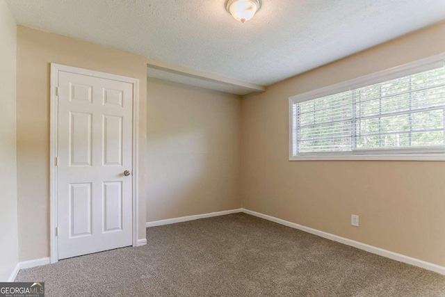 carpeted spare room featuring a textured ceiling and baseboards