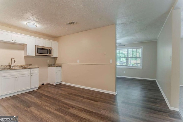 kitchen with a textured ceiling, dark wood-style flooring, visible vents, a sink, and stainless steel microwave