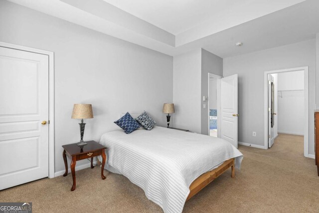 bedroom with light colored carpet, baseboards, and a walk in closet