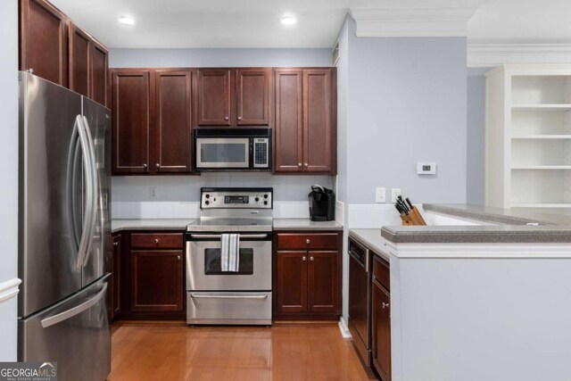 kitchen featuring stainless steel appliances, light wood-style floors, a peninsula, ornamental molding, and recessed lighting