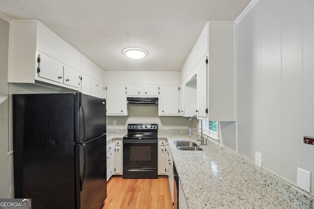 kitchen with a sink, black appliances, under cabinet range hood, white cabinetry, and light stone countertops