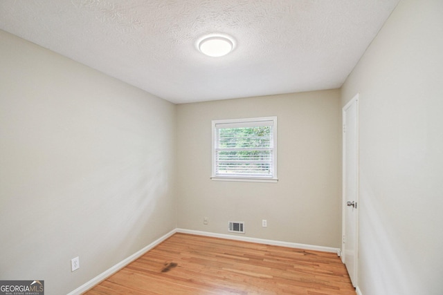 spare room with light wood-type flooring, baseboards, visible vents, and a textured ceiling