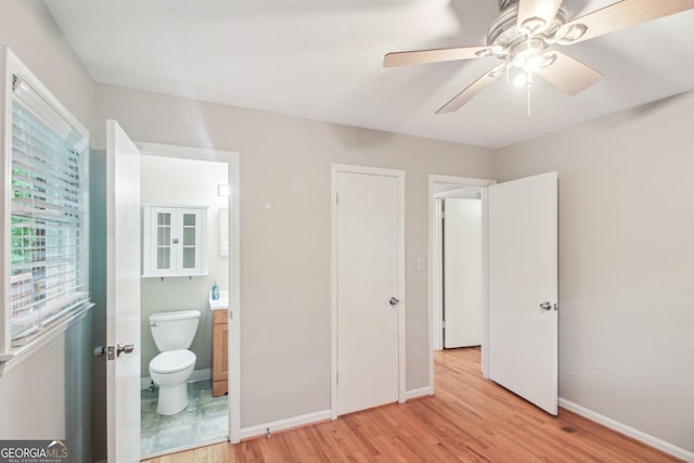 unfurnished bedroom featuring ensuite bath, light wood-style floors, baseboards, and a ceiling fan