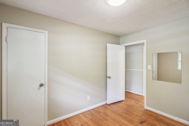 unfurnished bedroom with a textured ceiling, wood finished floors, and baseboards