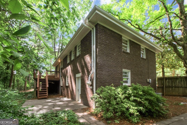 view of property exterior featuring brick siding, fence, a garage, stairs, and a deck