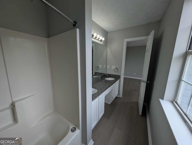 bathroom featuring a textured ceiling, double vanity, a sink, and wood finished floors