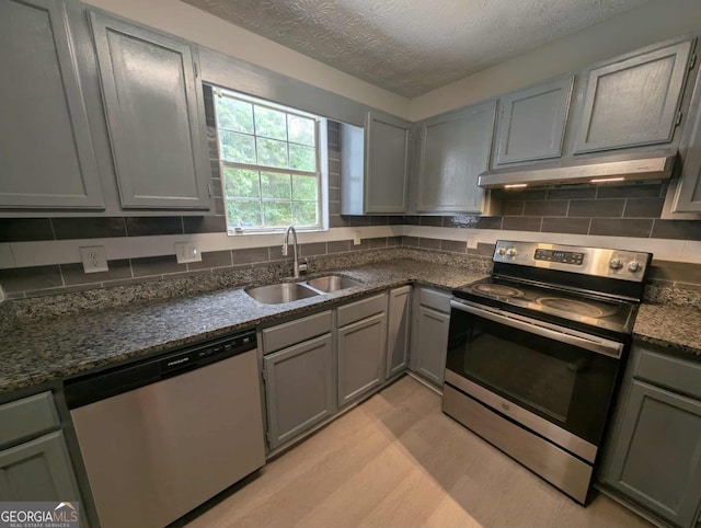 kitchen with gray cabinetry, under cabinet range hood, a sink, stainless steel appliances, and light wood-type flooring