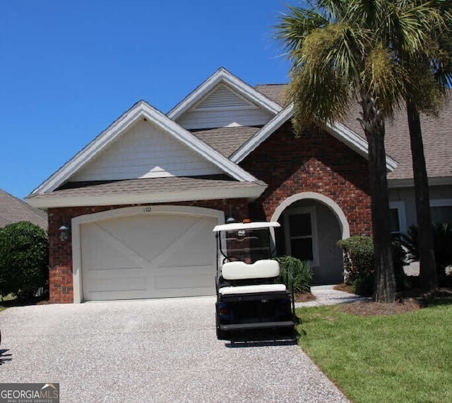 view of front of house with roof with shingles, an attached garage, brick siding, and driveway