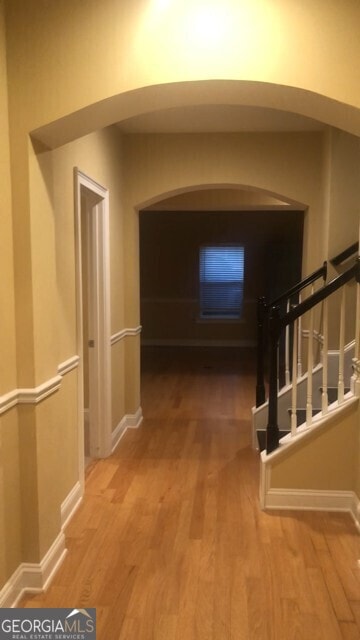 corridor with baseboards, arched walkways, and wood finished floors