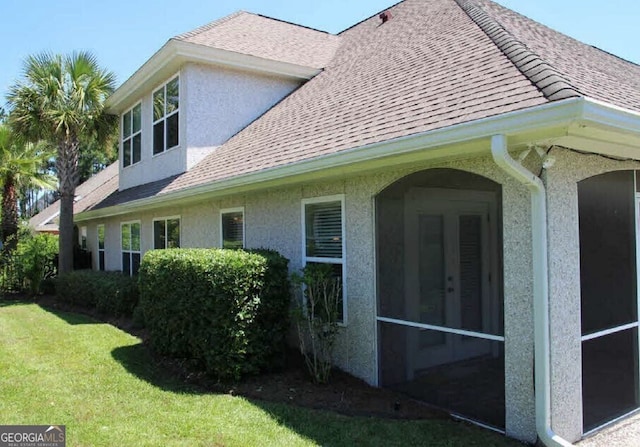 view of side of home with a shingled roof, stucco siding, and a lawn