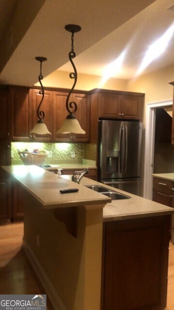 kitchen featuring light wood finished floors, a sink, decorative backsplash, stainless steel refrigerator with ice dispenser, and light countertops