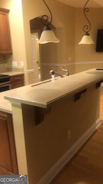 kitchen featuring brown cabinetry, light countertops, a breakfast bar area, and dark wood-style floors