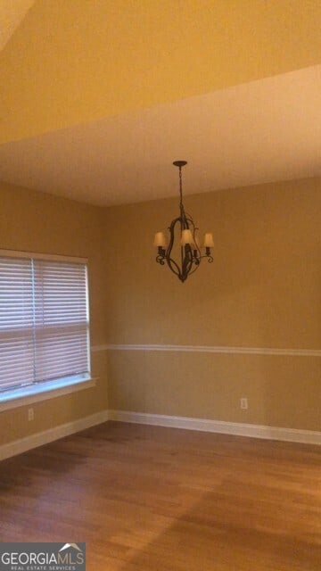 unfurnished room featuring a chandelier, wood finished floors, and baseboards