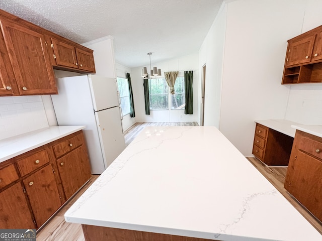 kitchen featuring freestanding refrigerator, brown cabinetry, open shelves, backsplash, and light wood-style floors