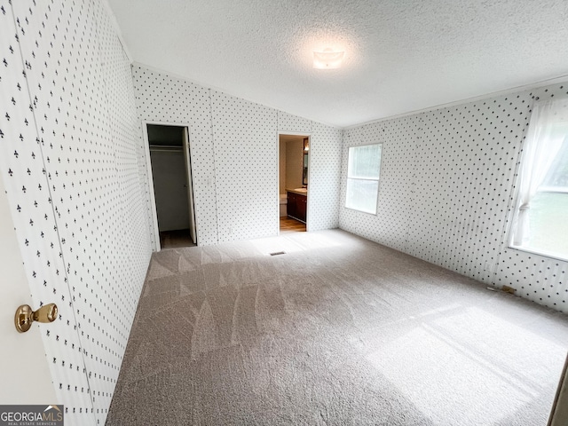 unfurnished bedroom featuring carpet flooring, wallpapered walls, a textured ceiling, ensuite bath, and lofted ceiling