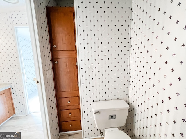 bathroom with toilet, wallpapered walls, and wood finished floors