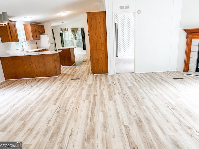unfurnished living room with a sink, a wealth of natural light, visible vents, and light wood-style floors