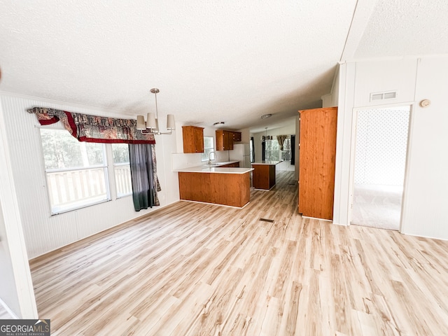 kitchen featuring a peninsula, brown cabinetry, a textured ceiling, open floor plan, and light wood-style floors