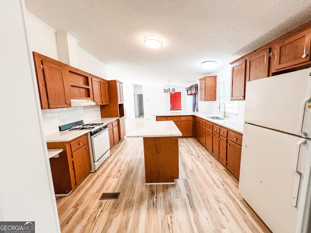 kitchen with under cabinet range hood, white appliances, visible vents, a sink, and a peninsula