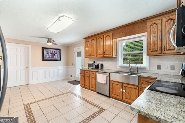 kitchen with stainless steel dishwasher, brown cabinetry, ceiling fan, a sink, and tasteful backsplash