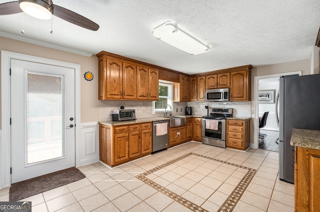 kitchen featuring a ceiling fan, a sink, stainless steel appliances, brown cabinetry, and decorative backsplash