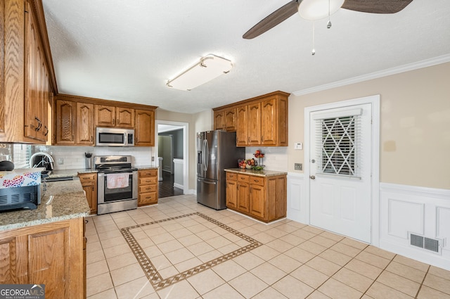 kitchen with a sink, stainless steel appliances, brown cabinetry, visible vents, and ceiling fan
