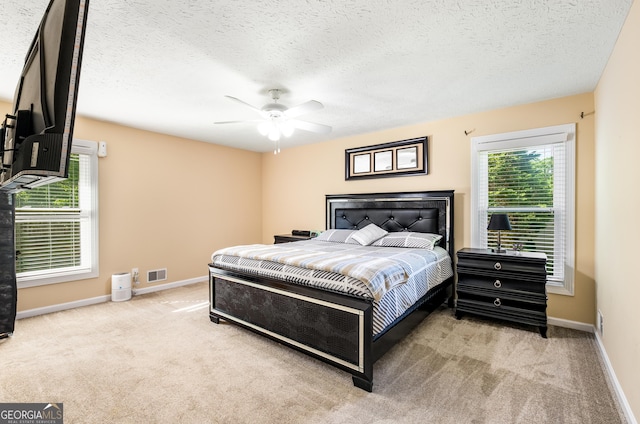 carpeted bedroom with a textured ceiling, baseboards, a ceiling fan, and visible vents