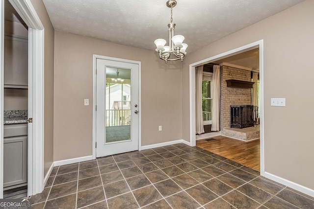 entryway featuring a textured ceiling, an inviting chandelier, a brick fireplace, dark tile patterned flooring, and baseboards