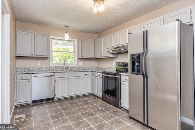 kitchen with a sink, stainless steel appliances, light stone counters, visible vents, and under cabinet range hood
