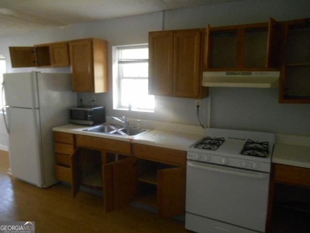 kitchen with under cabinet range hood, brown cabinetry, white appliances, a sink, and light countertops