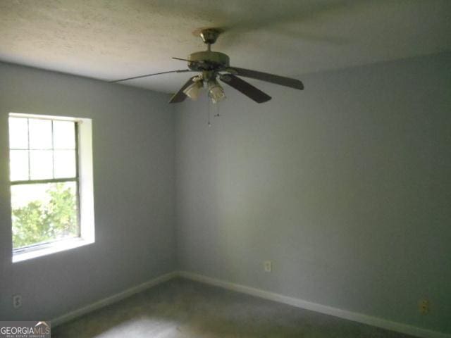 carpeted spare room featuring baseboards, a wealth of natural light, and a ceiling fan