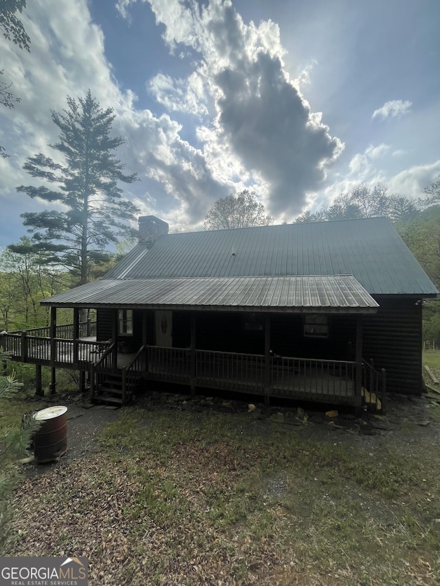 view of front of house with covered porch, a chimney, and metal roof