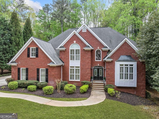 traditional-style house with a front yard, brick siding, and a shingled roof