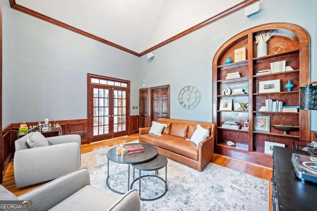 living area featuring wood finished floors, french doors, a wainscoted wall, ornamental molding, and high vaulted ceiling