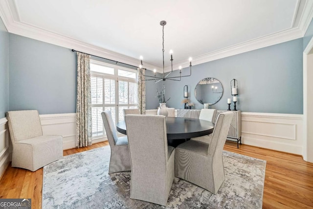 dining space with a chandelier, ornamental molding, wainscoting, wood finished floors, and a decorative wall
