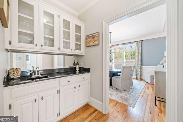 bar featuring a sink, ornamental molding, light wood-style flooring, and baseboards