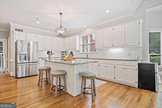 kitchen with stainless steel fridge with ice dispenser, white cabinets, a kitchen island, backsplash, and crown molding